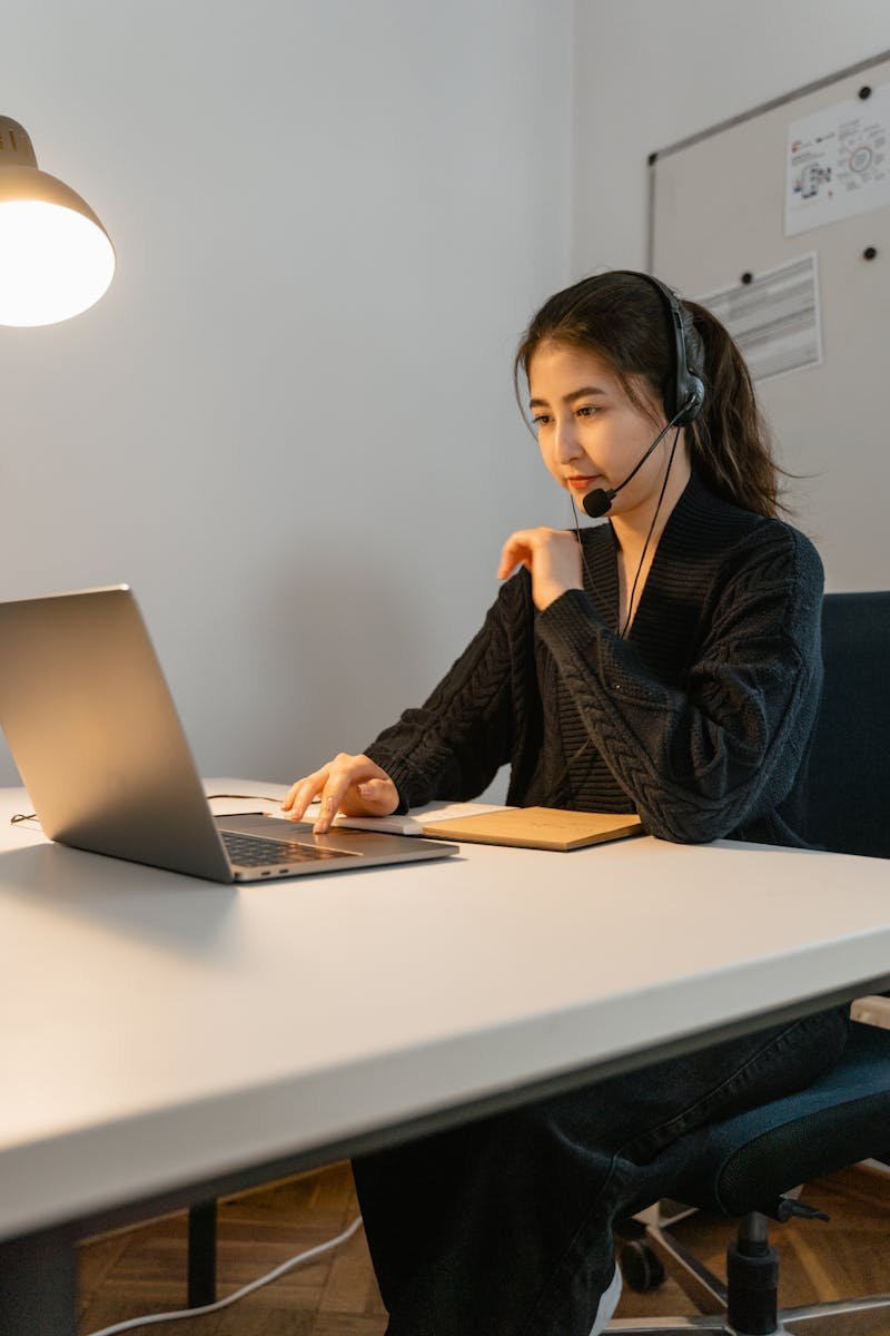 Asian woman in headset working on a laptop. Ideal for customer support themes.